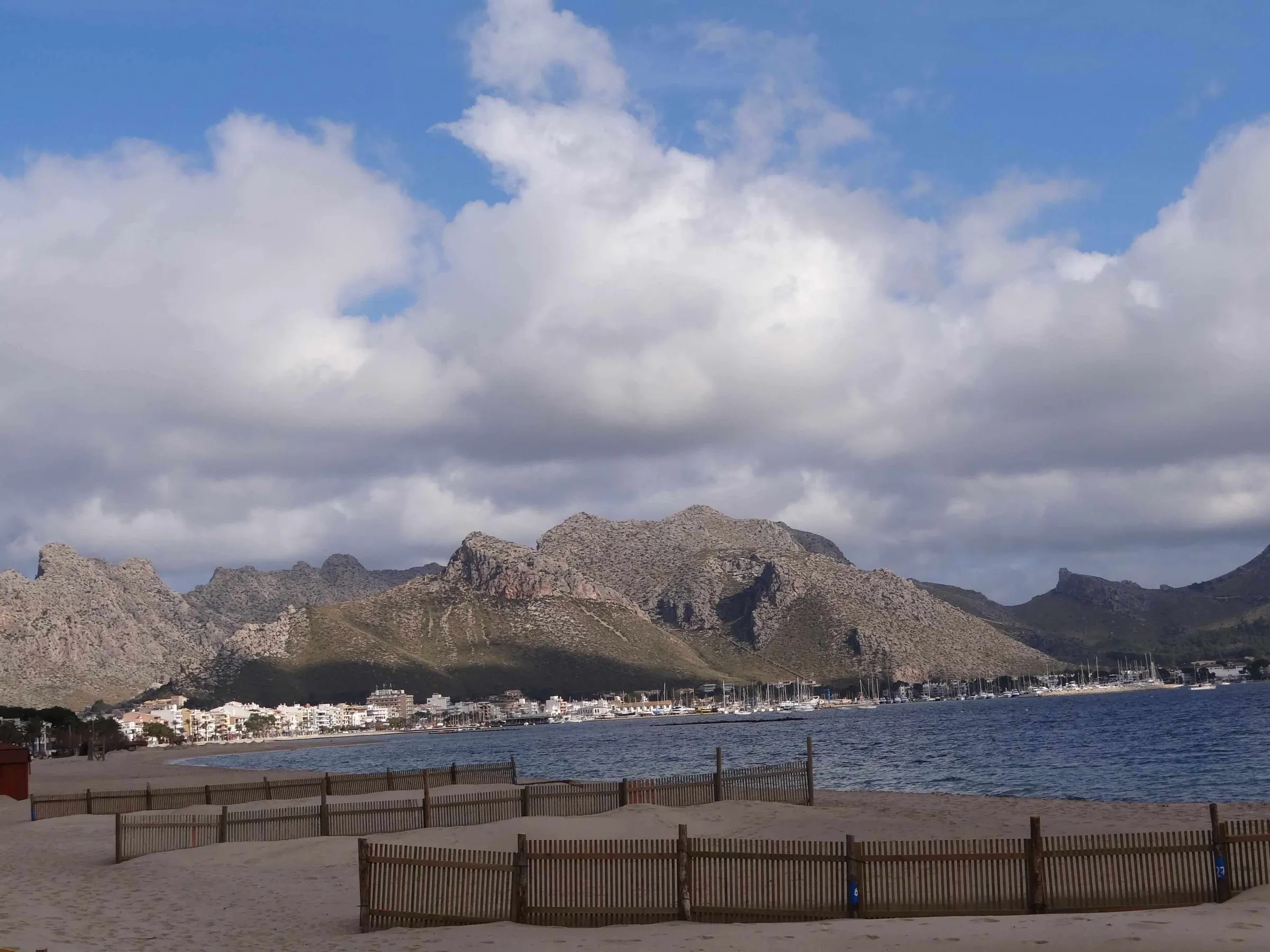 Sand von Llenaire mit Schutzzäunen, dahinter Port de Pollença am Fuß der Berge