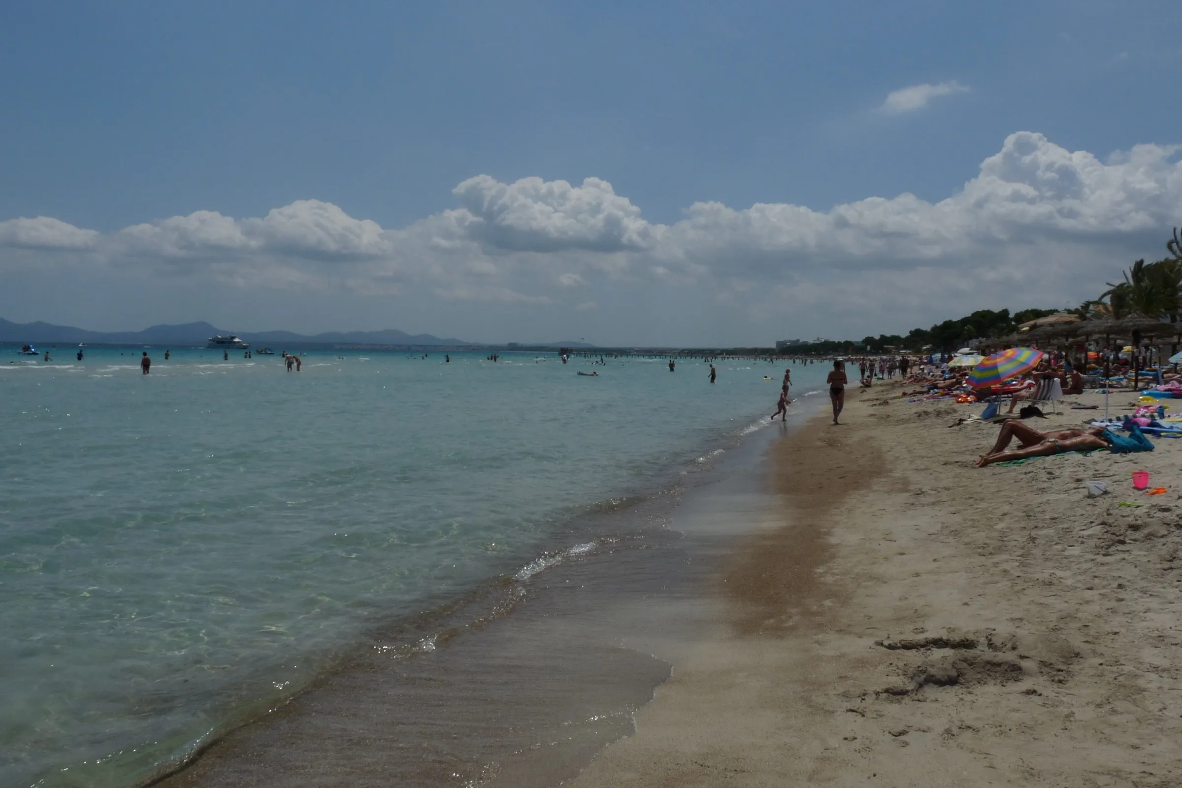 La orilla de la playa se pierde a lo lejos, con gente bañándose en agua poco profunda