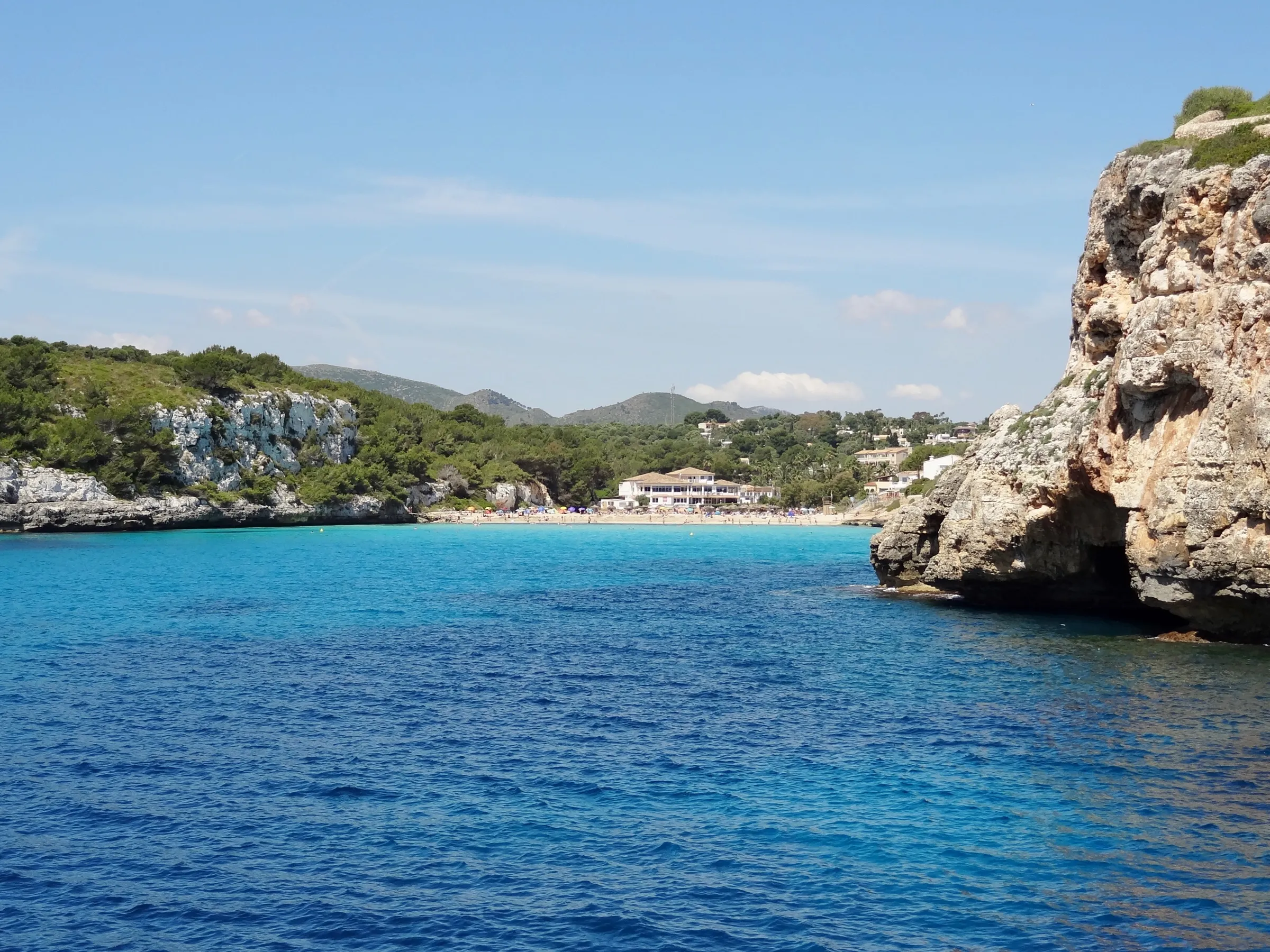 Pared de roca caliza en la entrada de la cala, con la playa y la urbanización al fondo