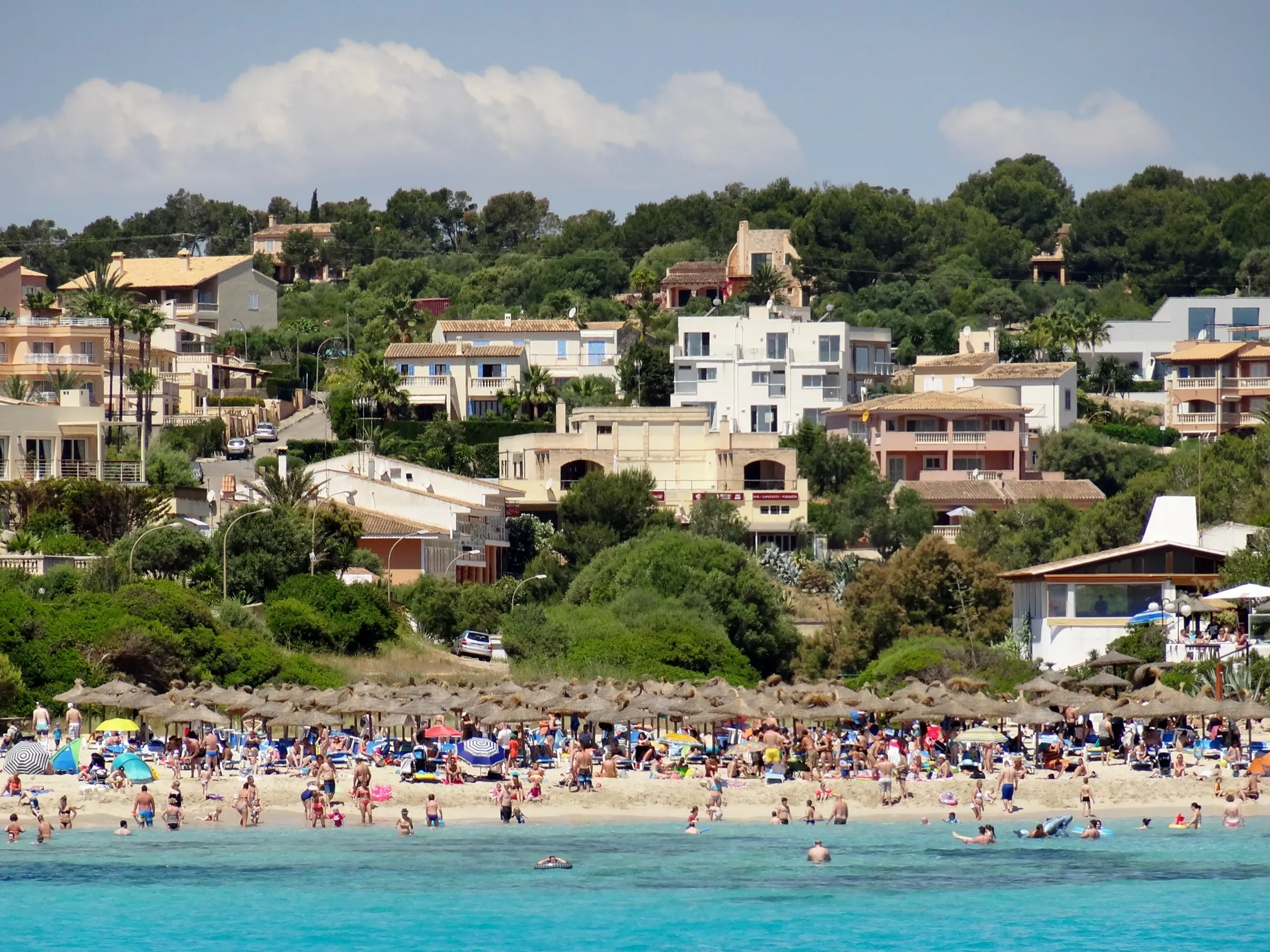 Bañistas en la orilla de Cala Mendia, con las casas y los hoteles de la urbanización en la ladera