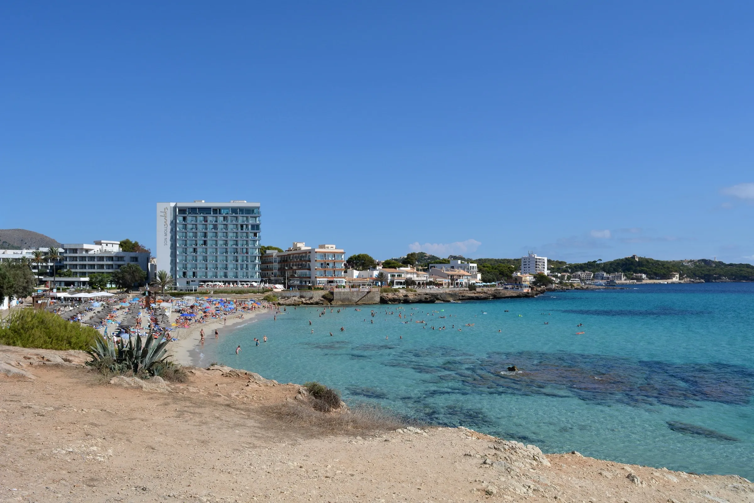 Son Moll vista desde las rocas del sur, con el agua clara y los hoteles de Cala Rajada al fondo