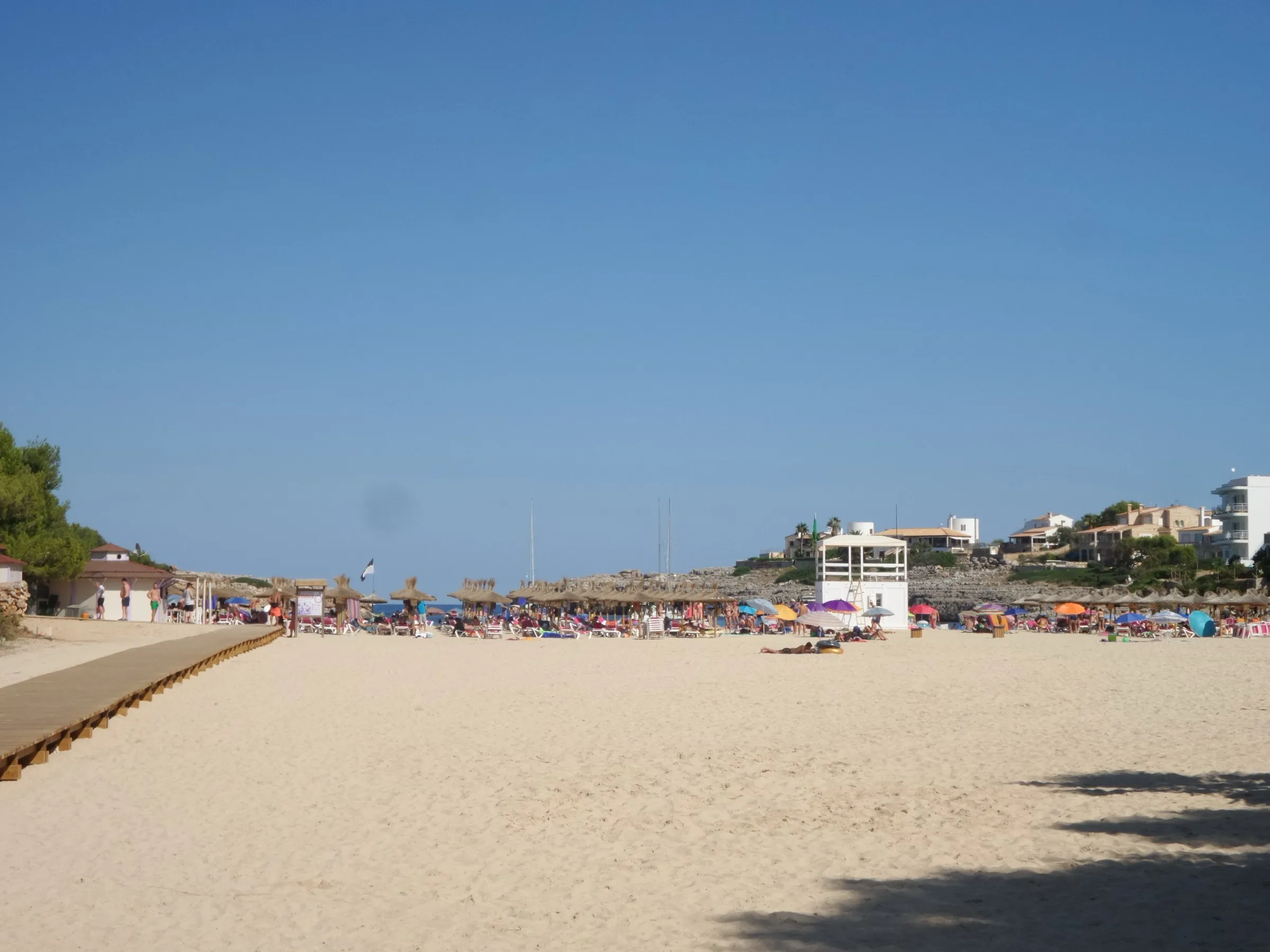 La arena de Cala Marçal con la pasarela de madera, la torre del socorrista y las sombrillas