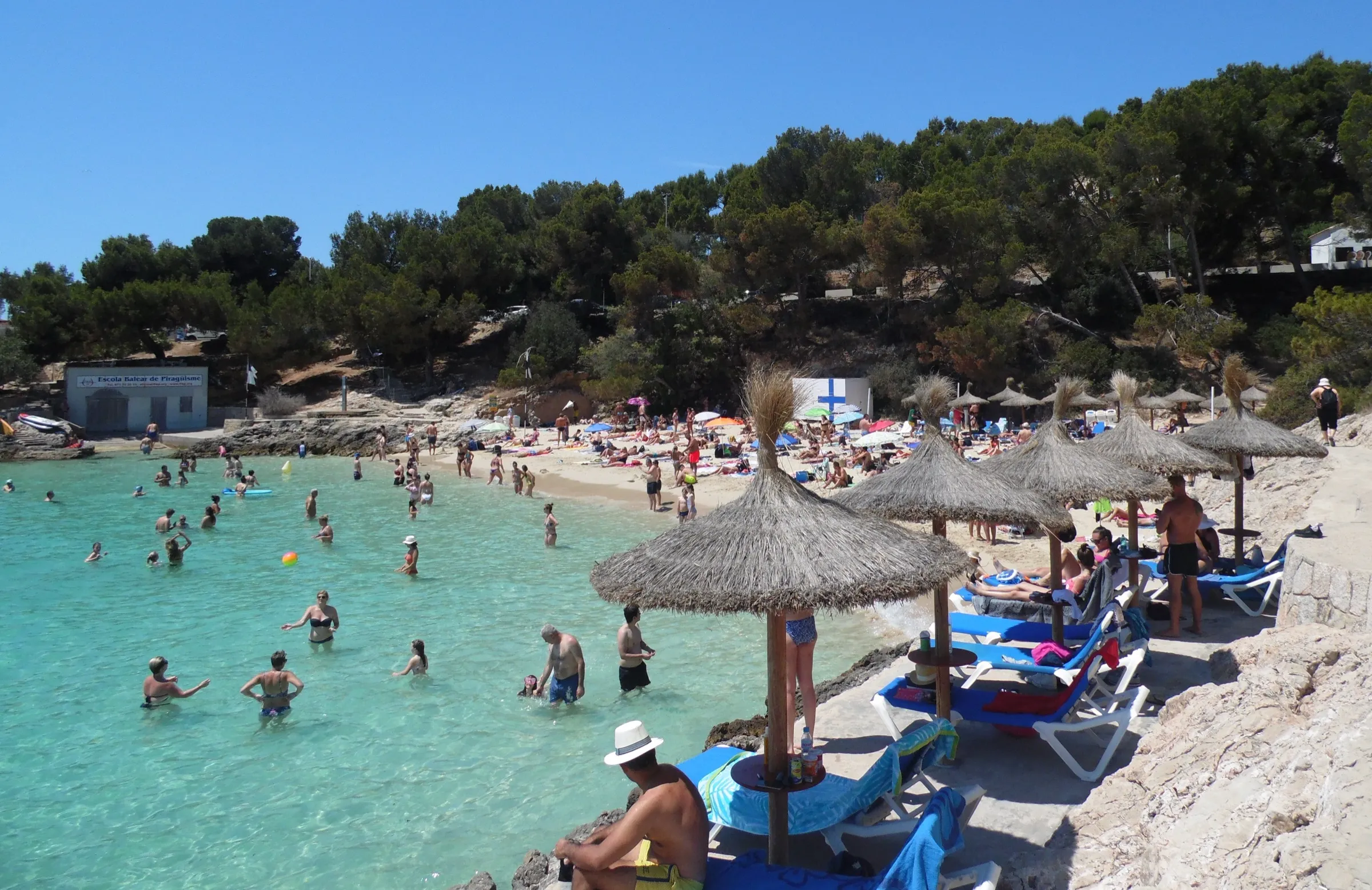 Bañistas en el agua de Cala Comtesa, con sombrillas de paja y hamacas en primer plano