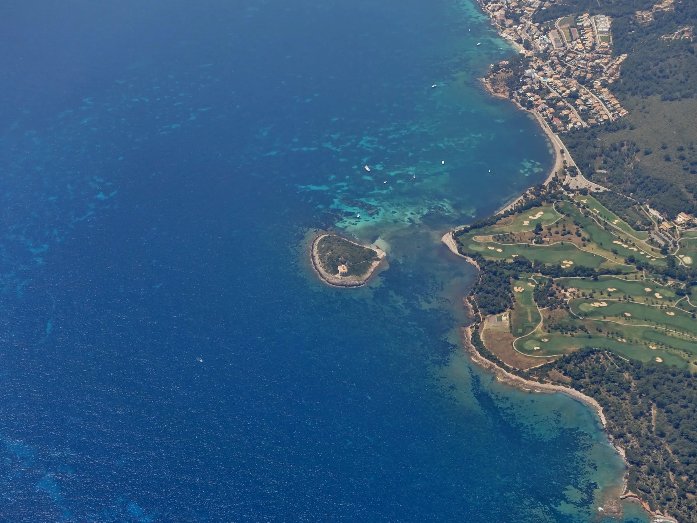 Aerial view of the Alcanada islet and the coast, with the pale seabed of the bay