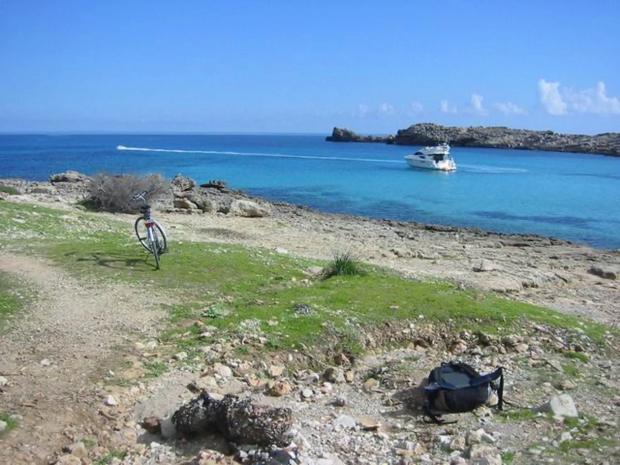 Sendero sobre la roca junto a Cala Moltó, con el mar azul y una lancha frente a la punta