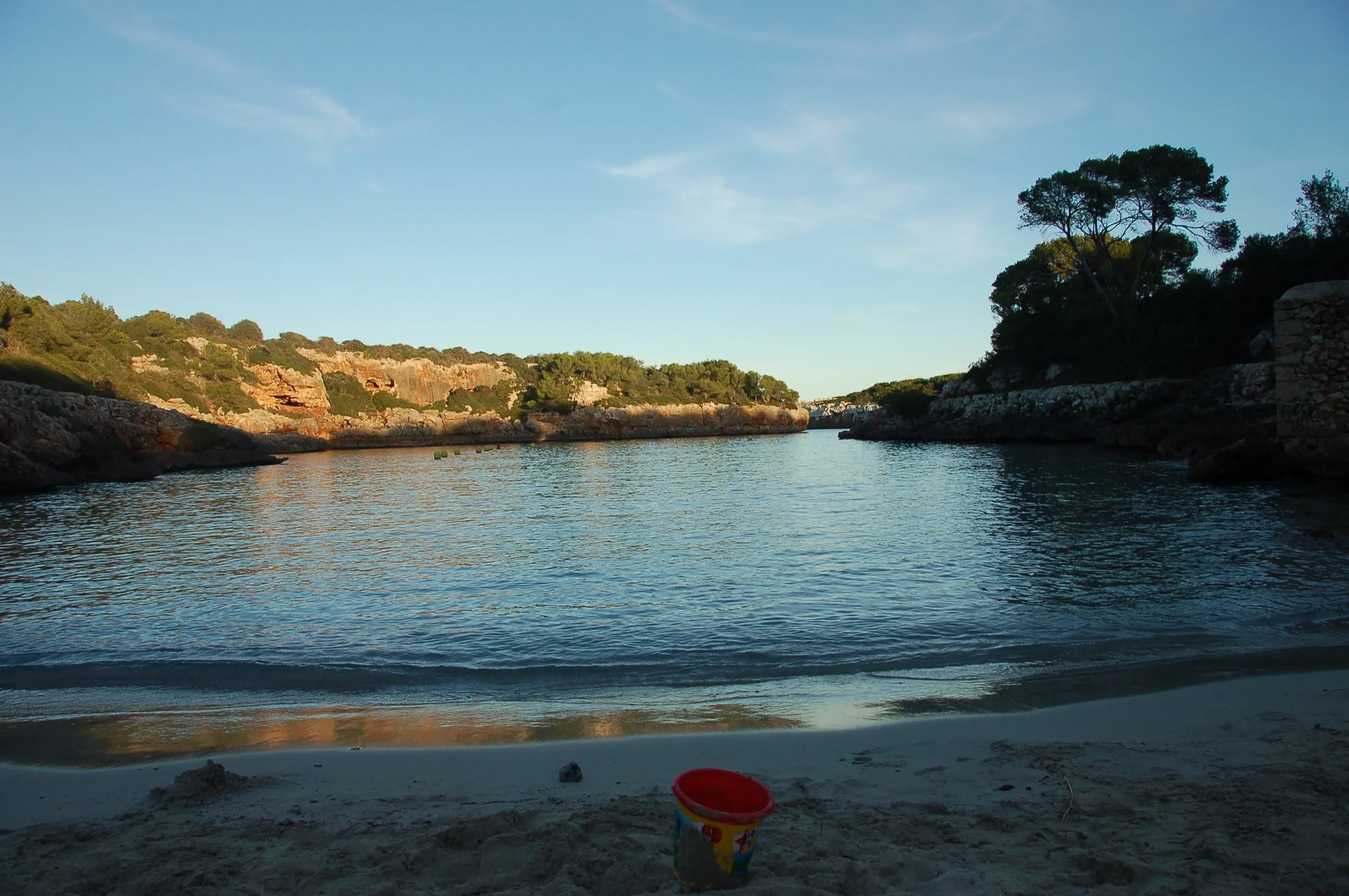 Vista desde la orilla de Cala Sa Nau hacia la salida al mar, con el agua en calma al atardecer