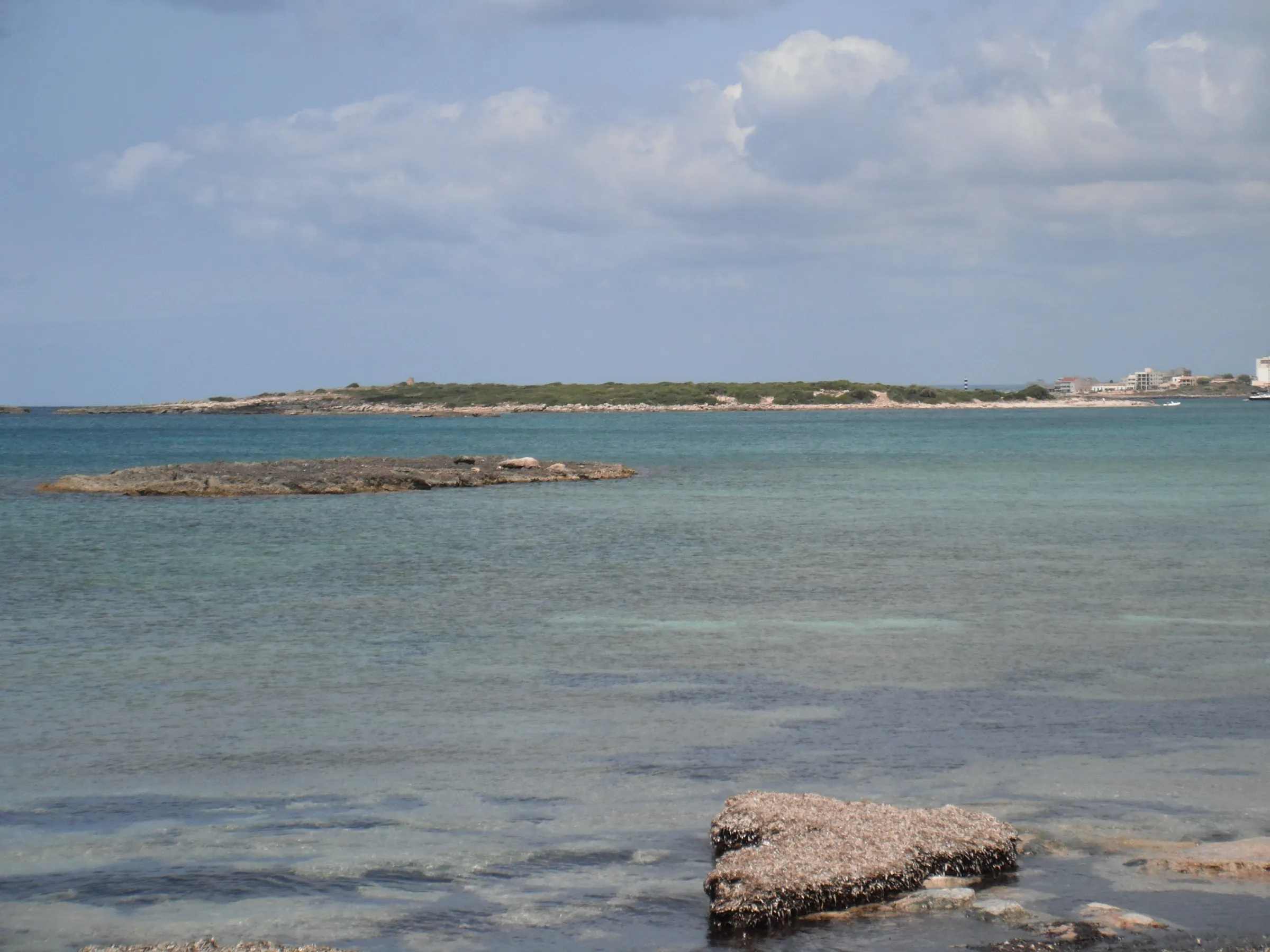 Vista desde es Carbó hacia el islote de na Moltona, con rocas en la orilla y agua clara