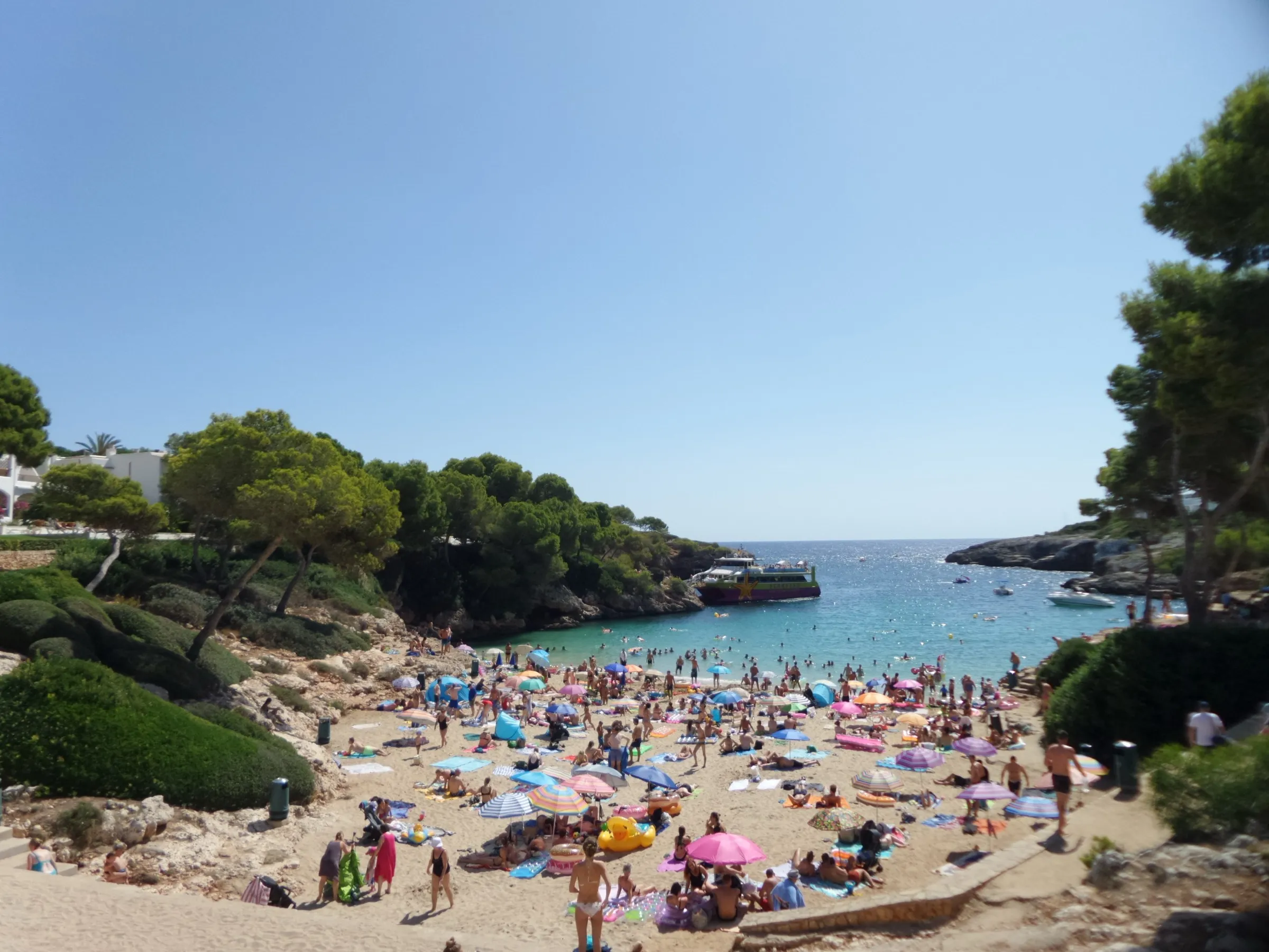 Cala Esmeralda llena de sombrillas y bañistas en pleno verano, vista desde el camino de bajada