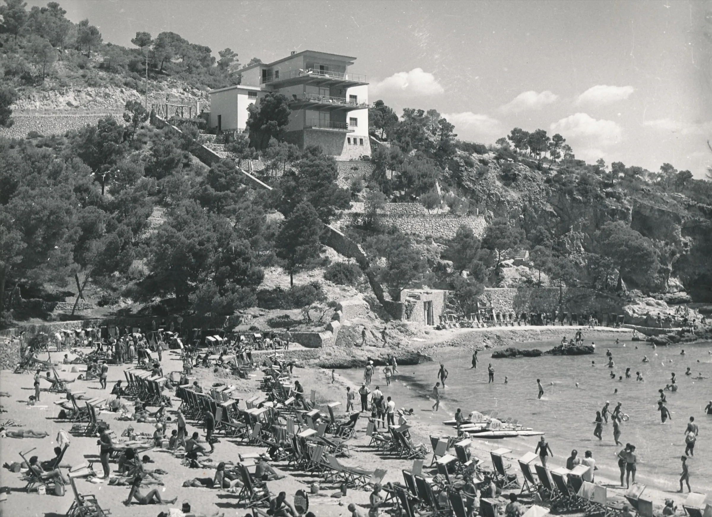 Fotografía en blanco y negro de la playa de Illetes en 1960, llena de bañistas y hamacas