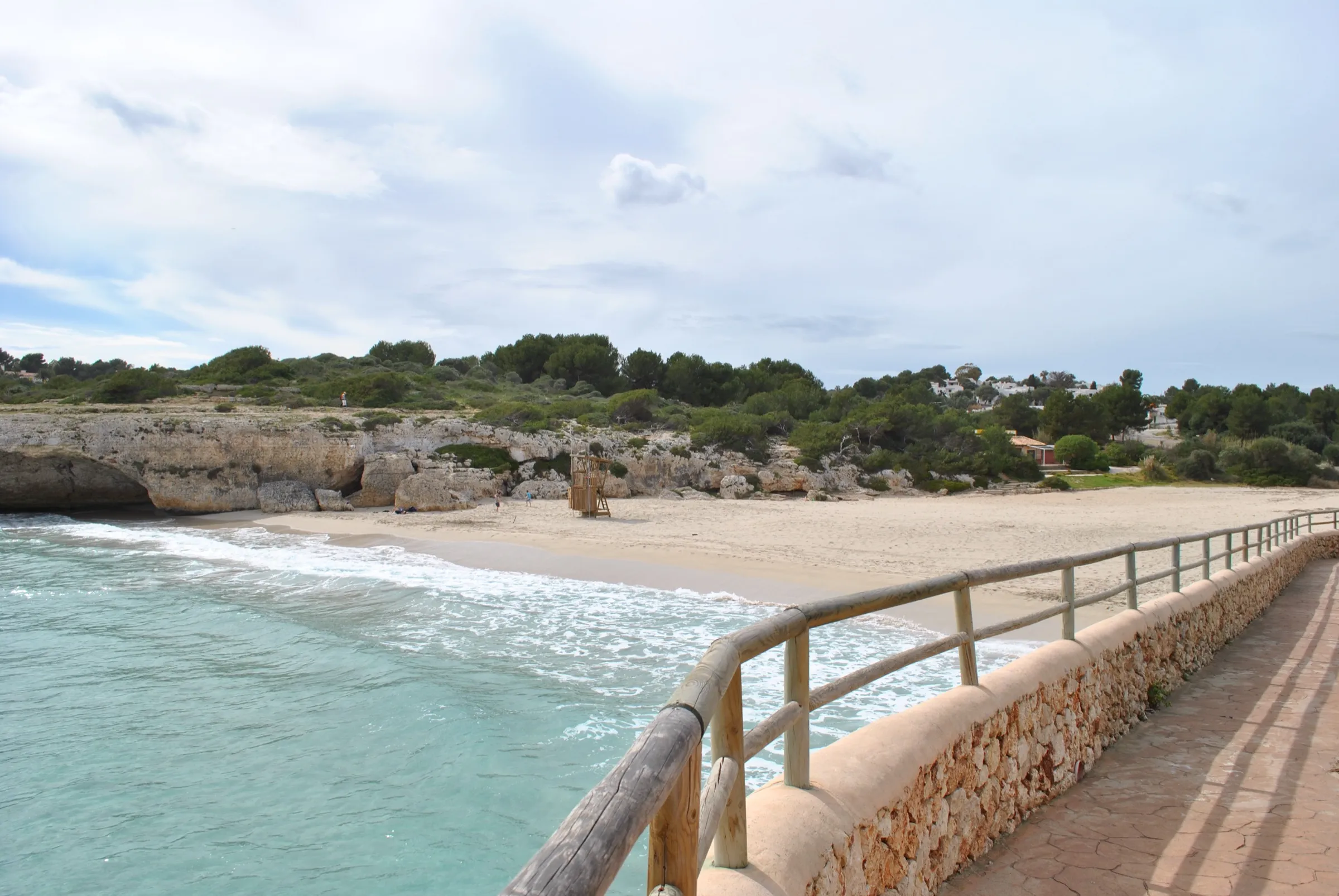 Pasarela con barandilla de madera que baja junto a la roca hasta la arena de Cala Domingos