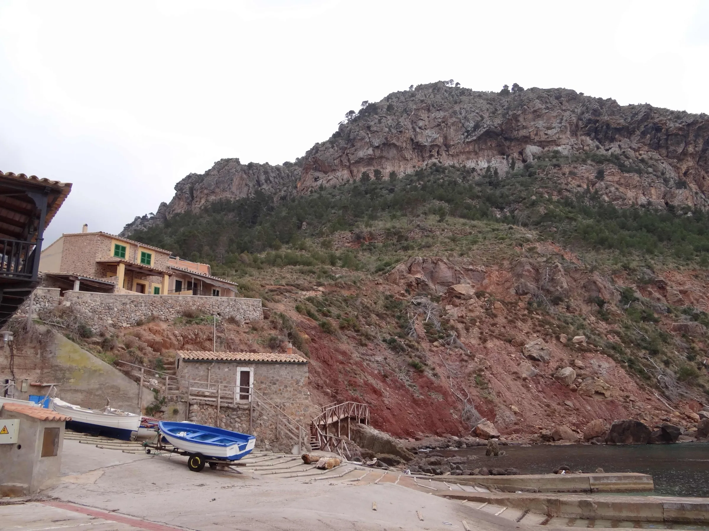 La rampa del Port de Valldemossa con barcas varadas sobre la grava, bajo casas de piedra y una ladera rocosa