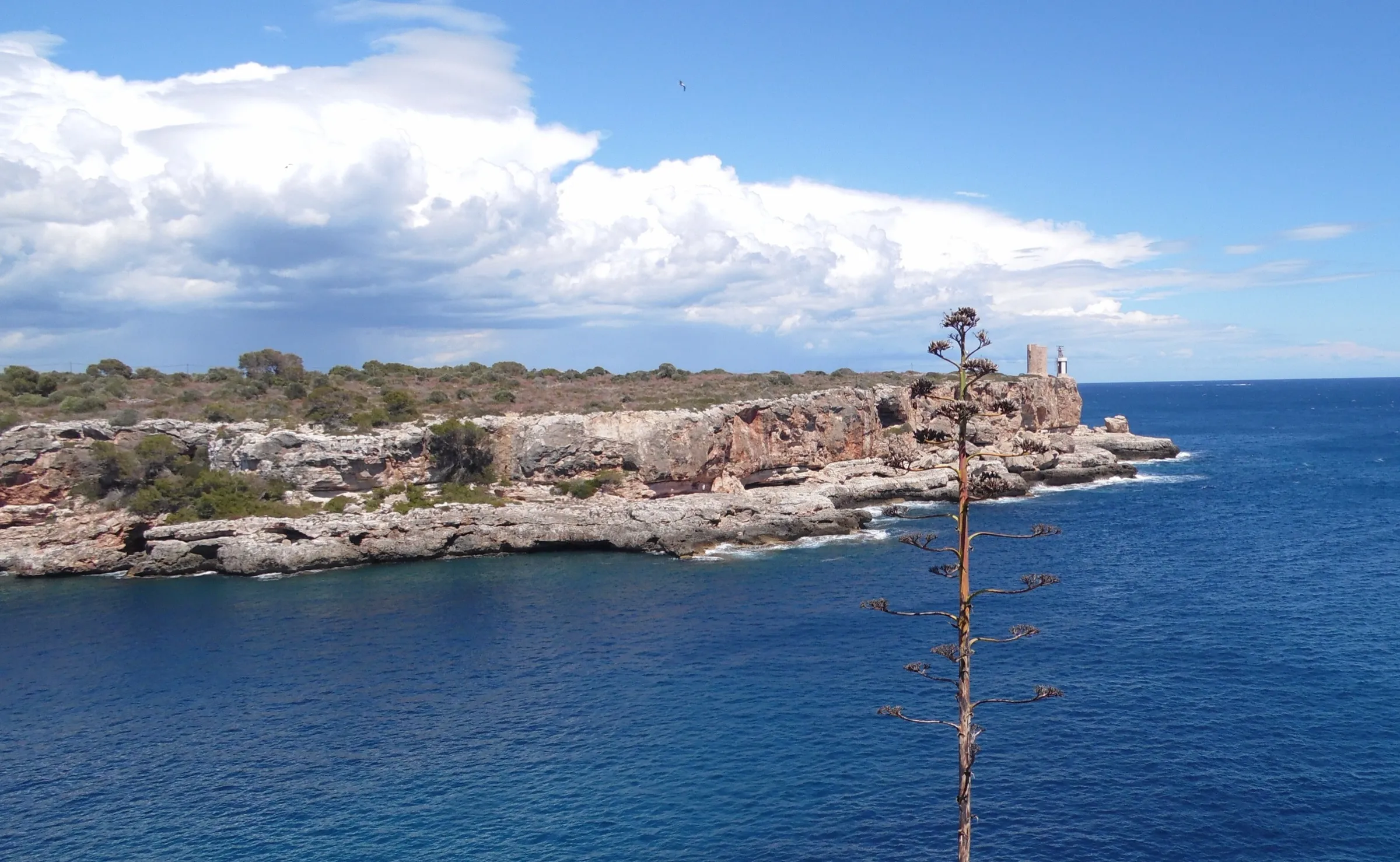Cliffs at the mouth of Cala Figuera opening onto the sea, with a building on the headland
