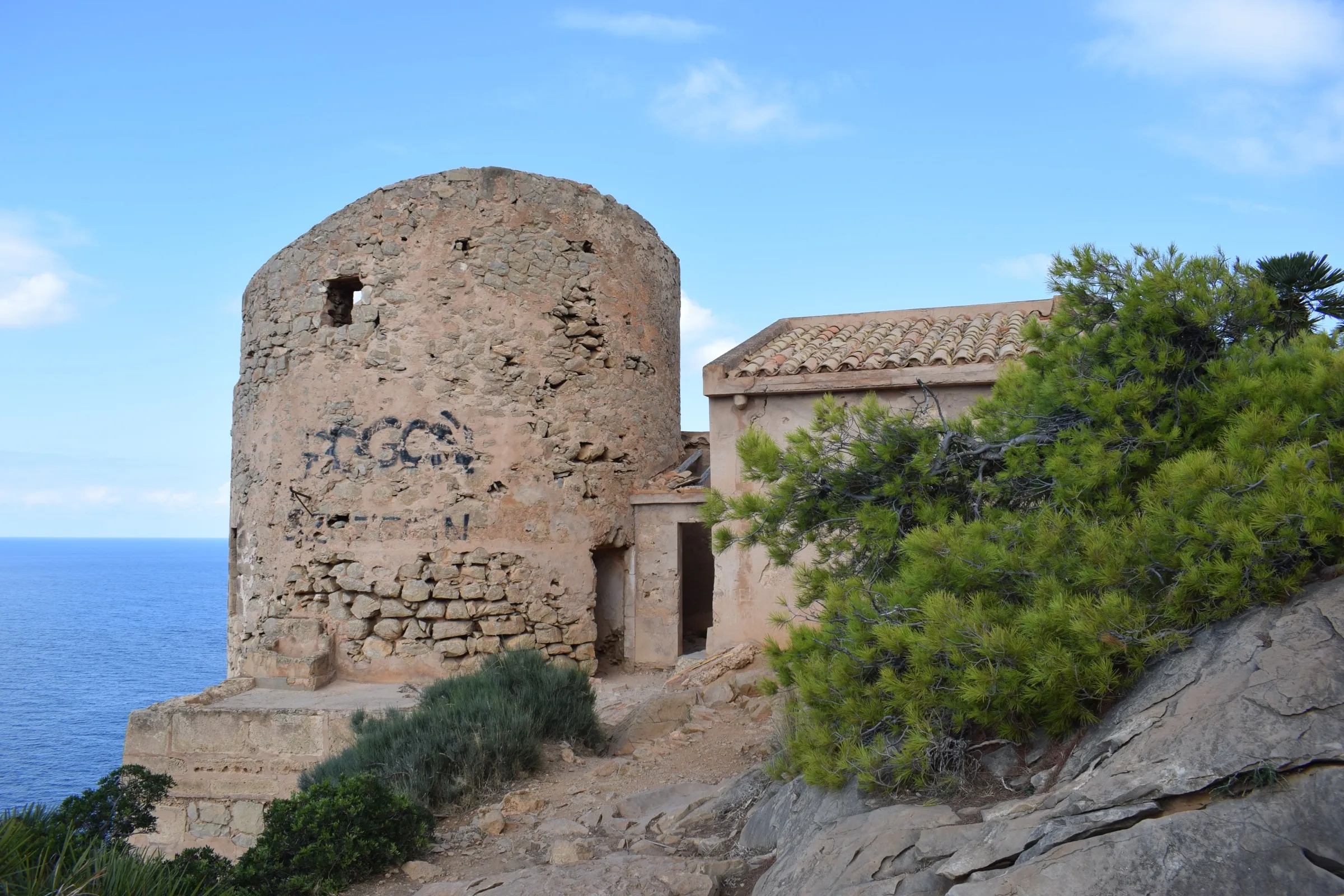 La torre de defensa de Cala en Basset, de piedra, junto a la caseta adosada