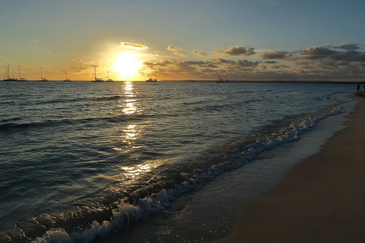 Puesta de sol desde la orilla de Es Trenc, con veleros fondeados en la bahía