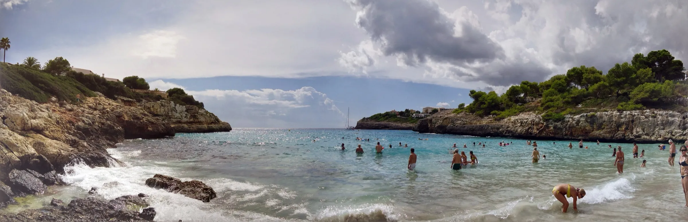 Bañistas en el agua poco profunda de Cala Anguila, mirando hacia la salida de la cala entre dos puntas de roca
