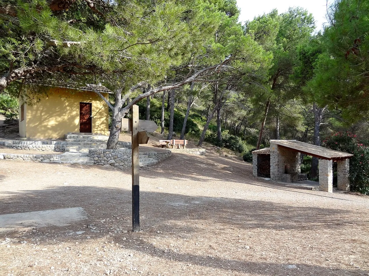 Refugio de es Coll Baix entre pinos, con mesas y un poste indicador del sendero