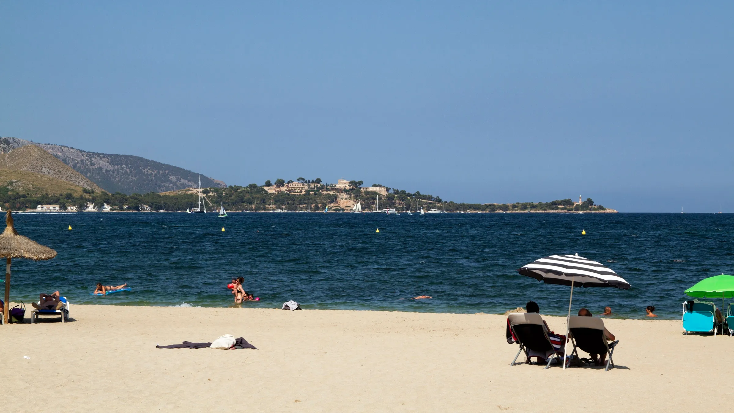 Swimmers on the sand at Llenaire looking out over the bay of Pollença, with the opposite coast in the distance