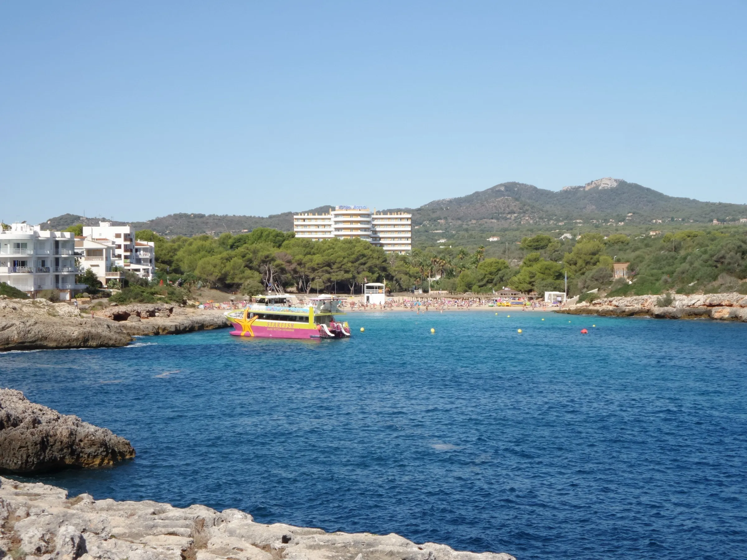 La entrada de Cala Marçal vista desde las rocas de la boca, con una barca de excursiones y la playa al fondo