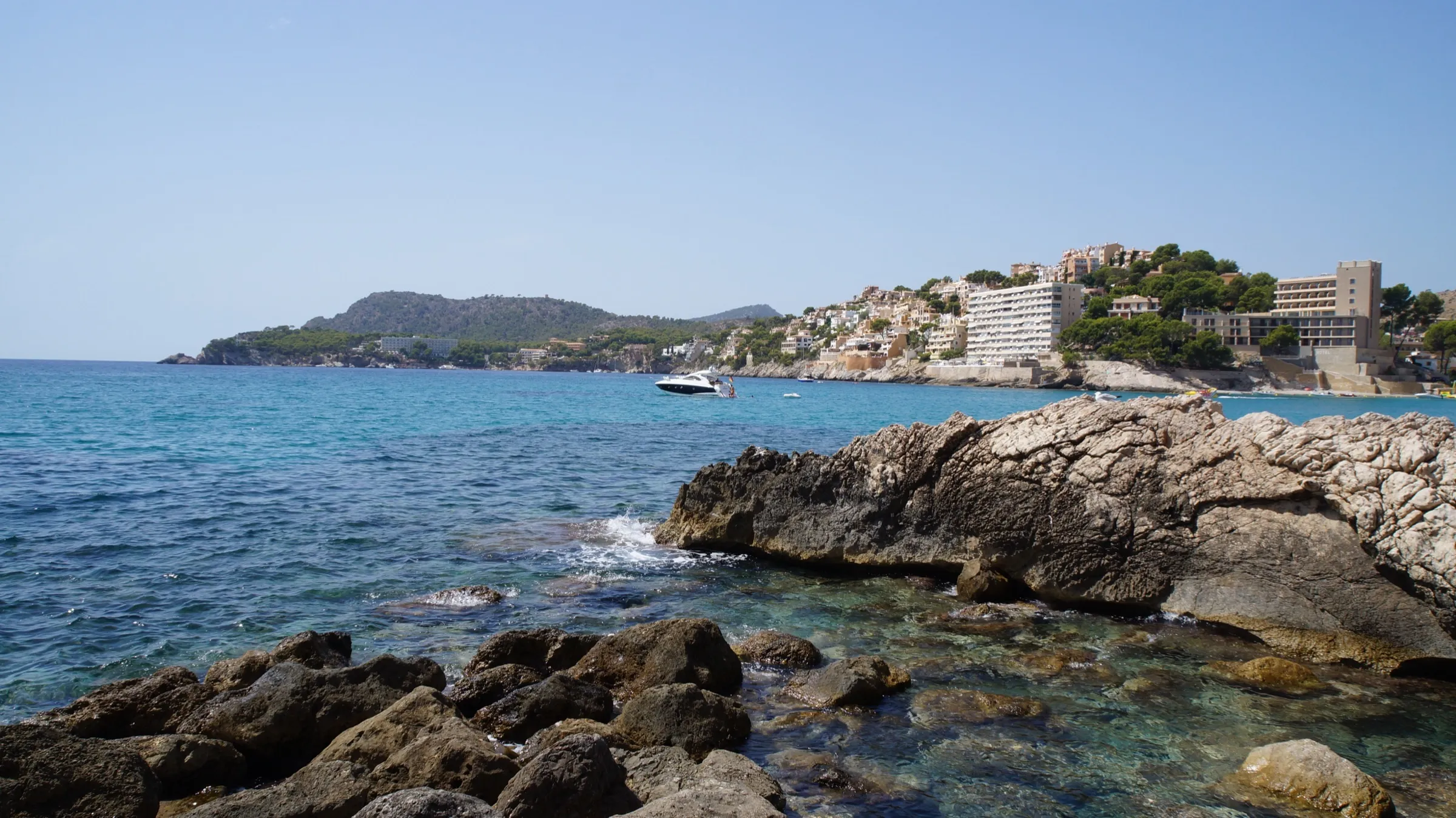 Rocks by clear water at the end of Cala Major, with the built-up coast of the bay behind