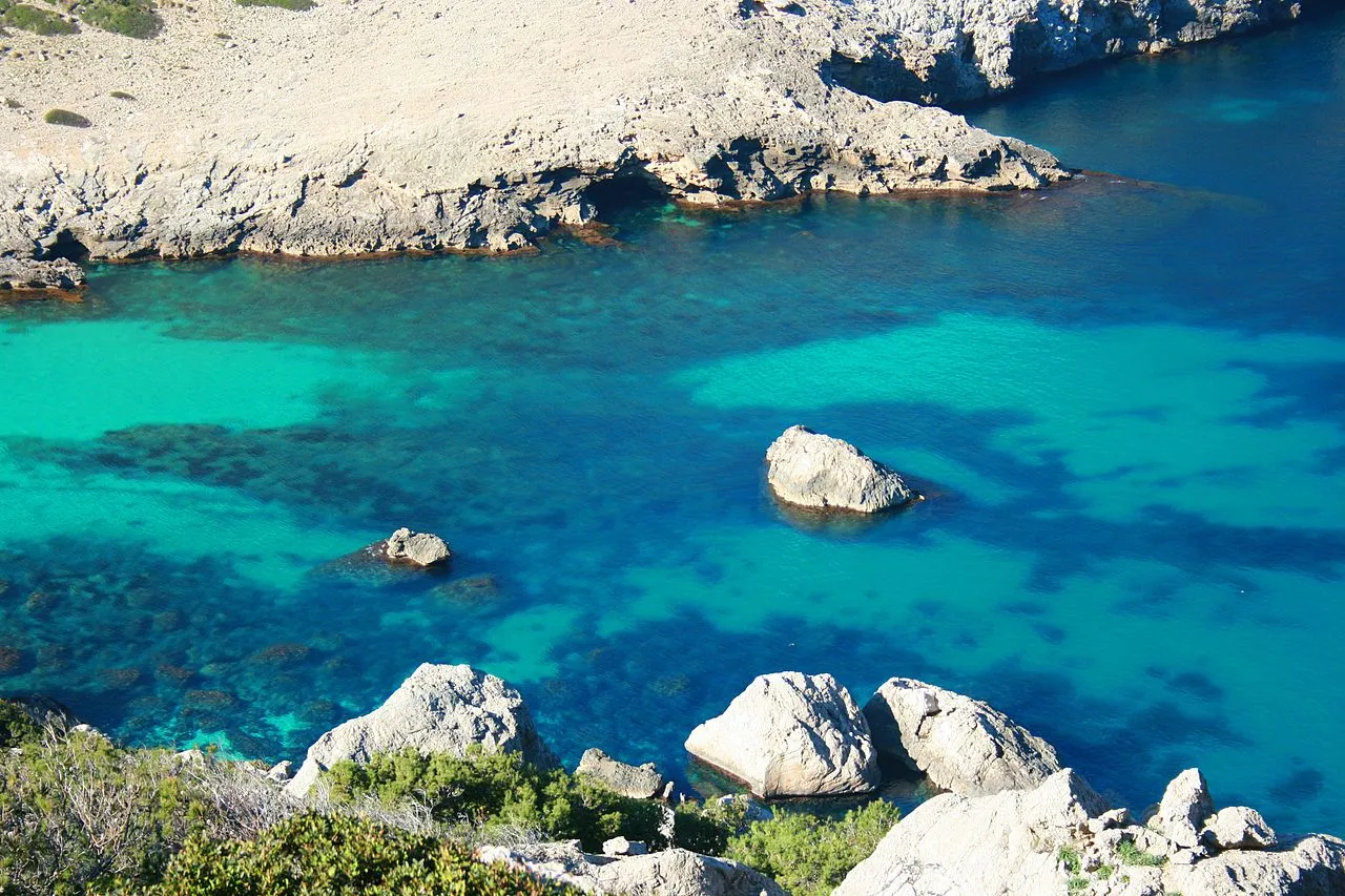 Agua turquesa con rocas sueltas y manchas de posidonia en Cala Figuera, vista desde arriba