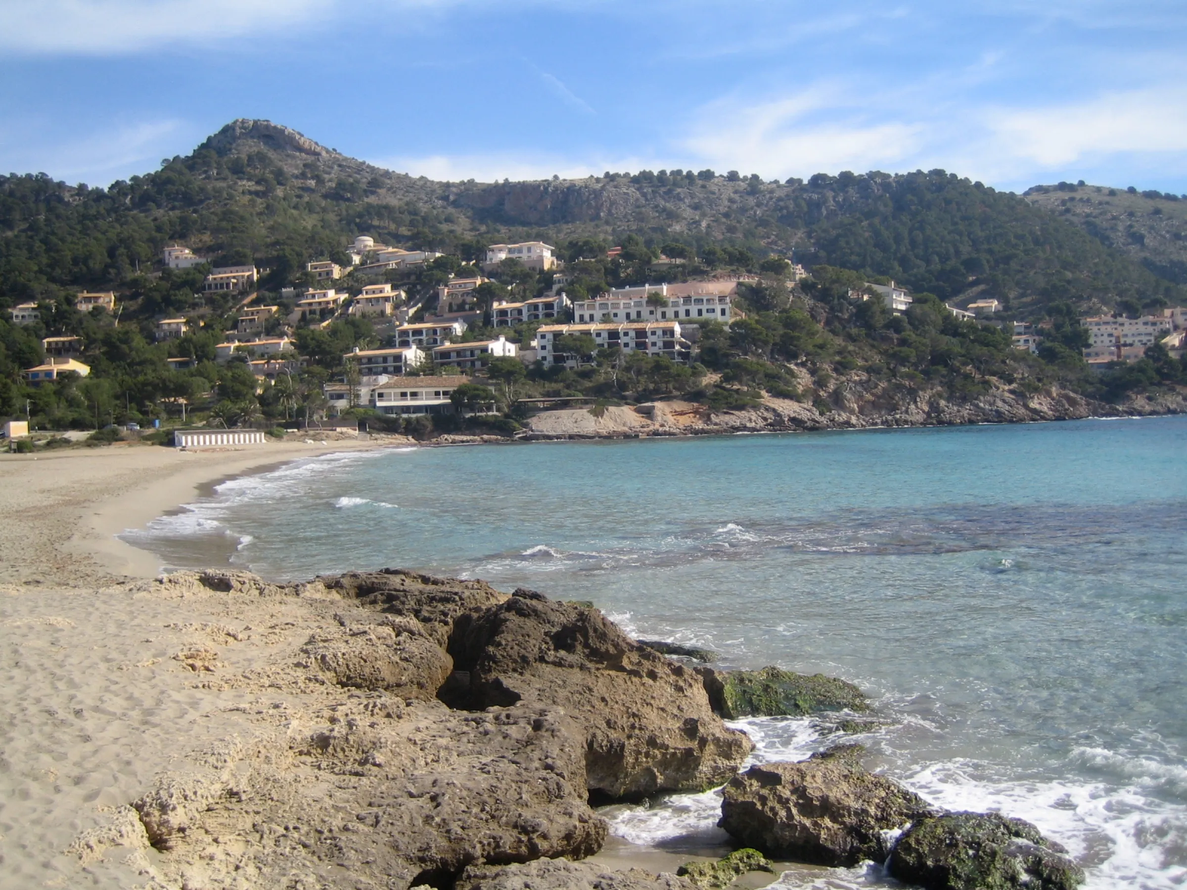 Rocks on the shore at Canyamel, with the sand and the slopes of Cap Vermell in the background