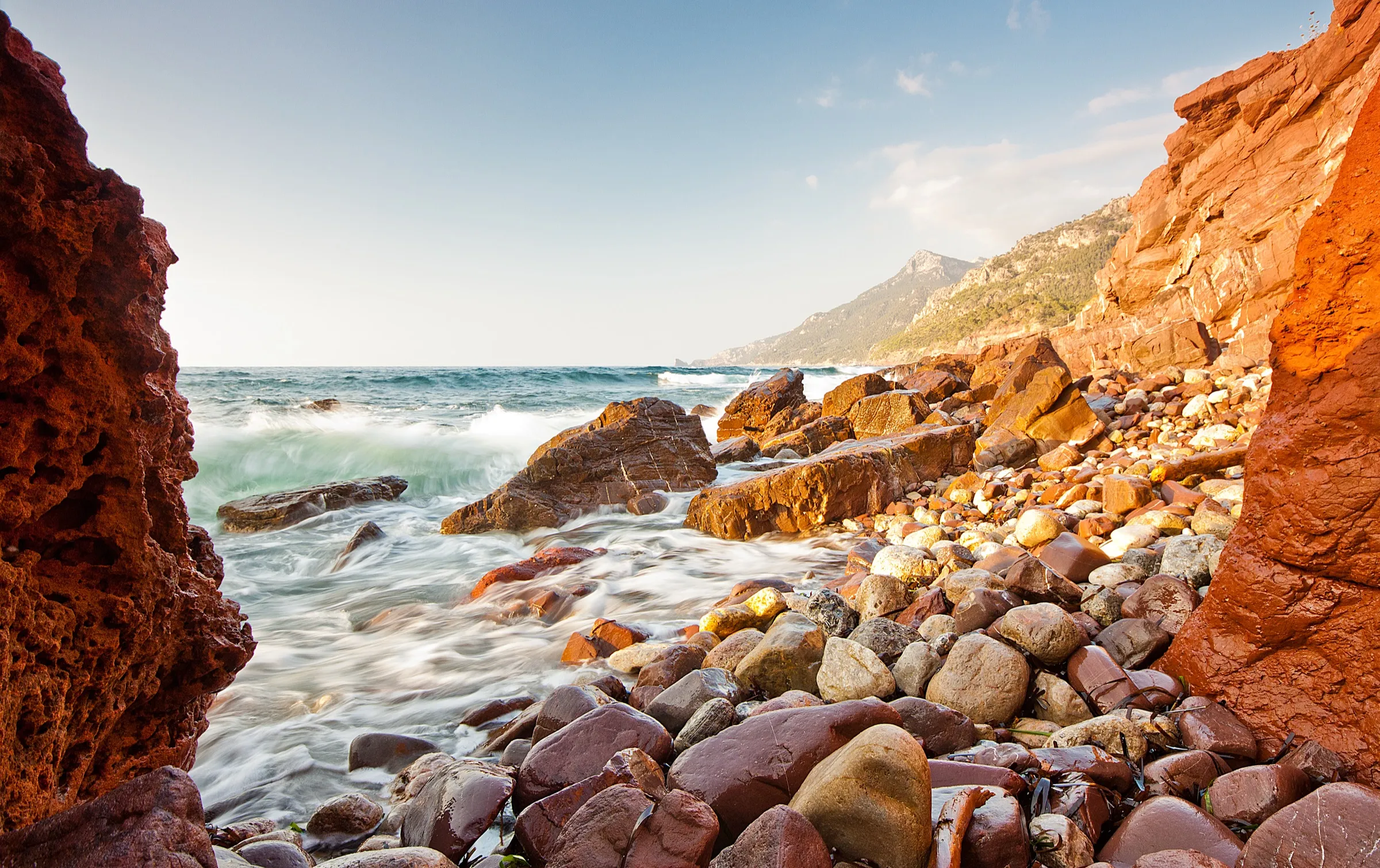 Rocas y cantos rojizos del Port des Canonge con el mar en movimiento, en una foto de larga exposición