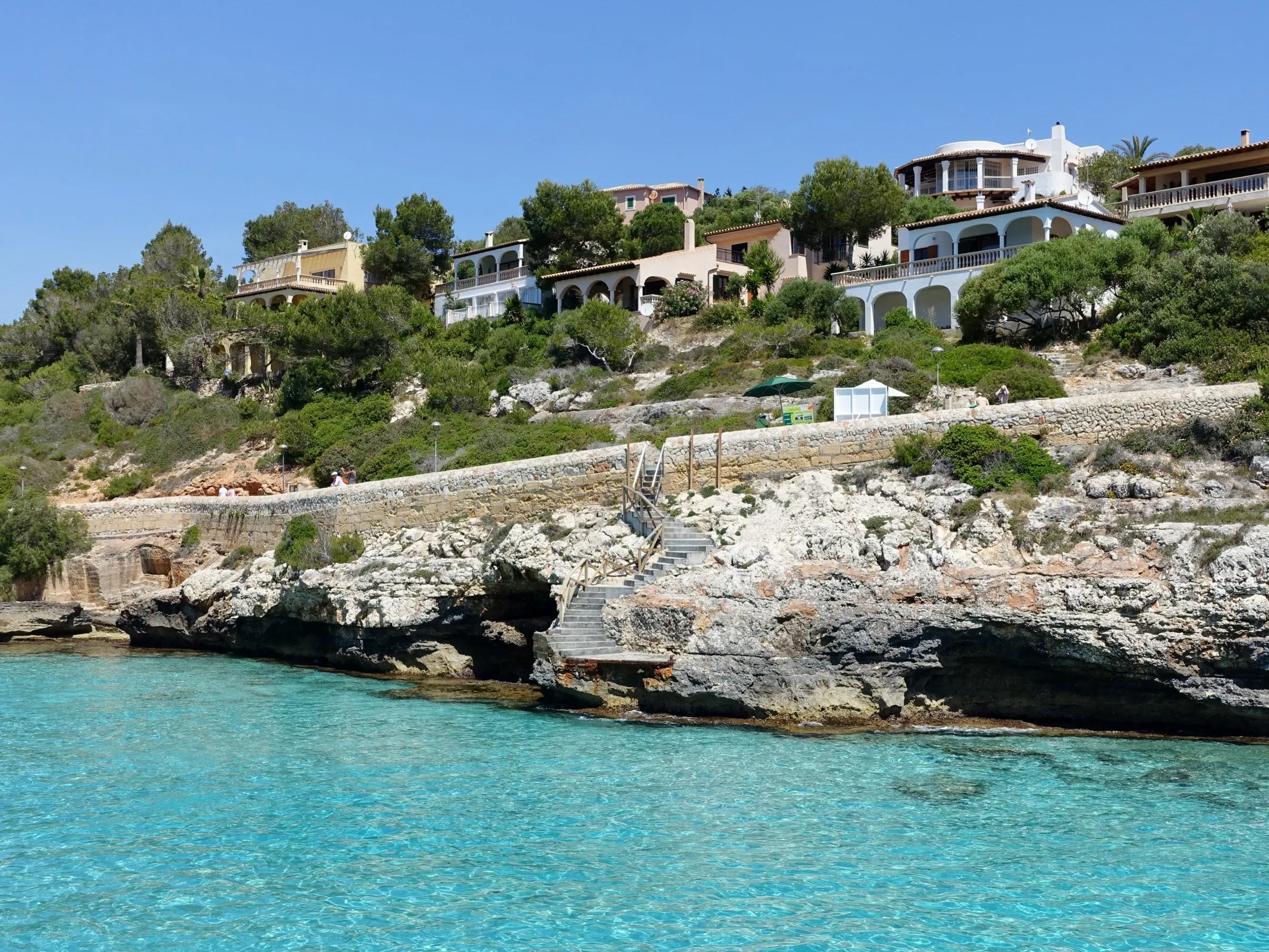 Rocas bajas en un lateral de la cala, con casas blancas entre los pinos