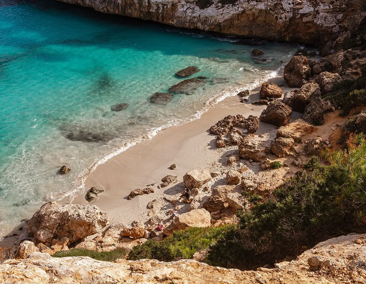 Orilla de arena y rocas del Caló des Moro vista desde arriba, con el agua turquesa