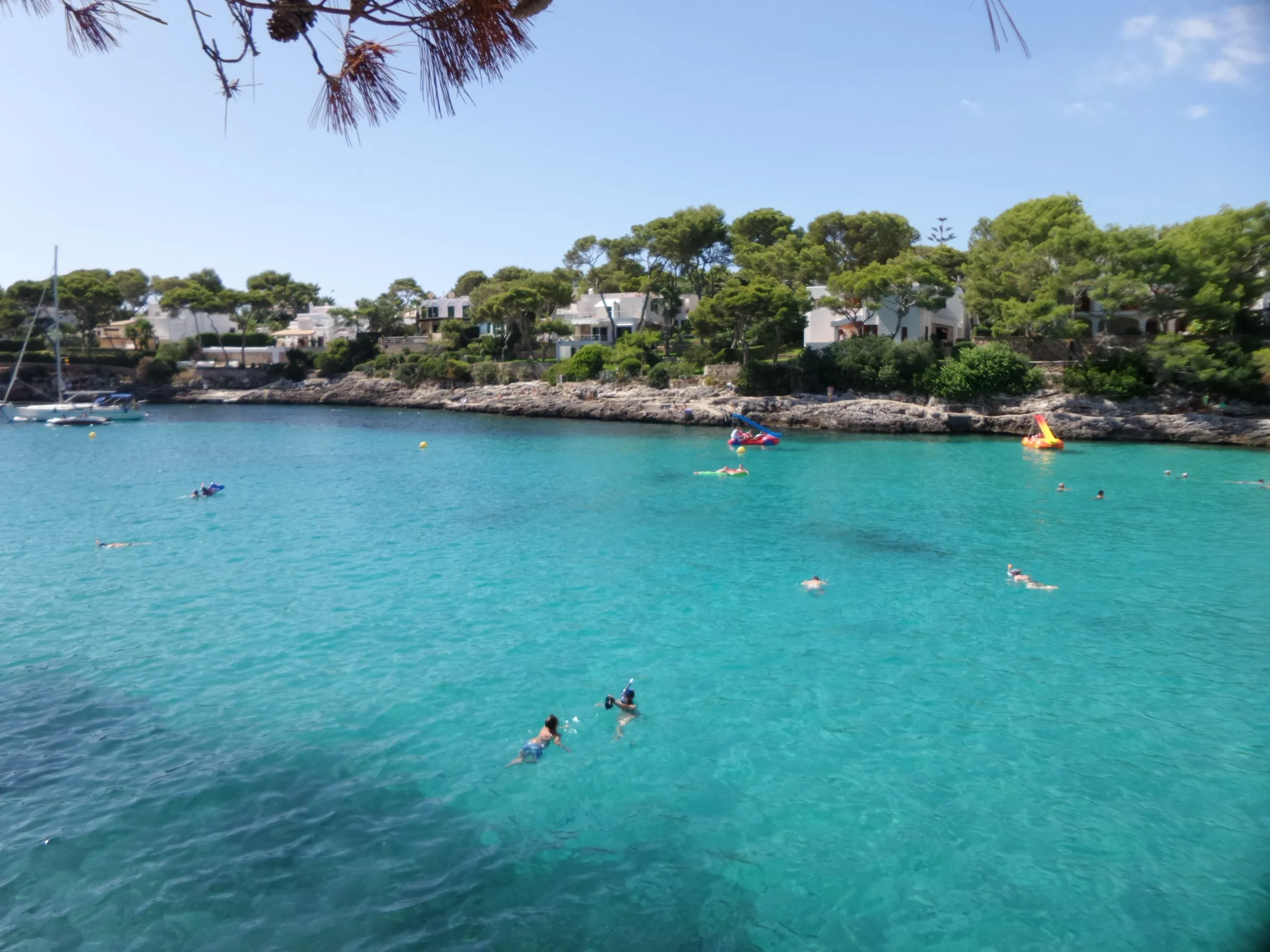 Clear turquoise water at Cala Gran, with swimmers and houses among the pines behind